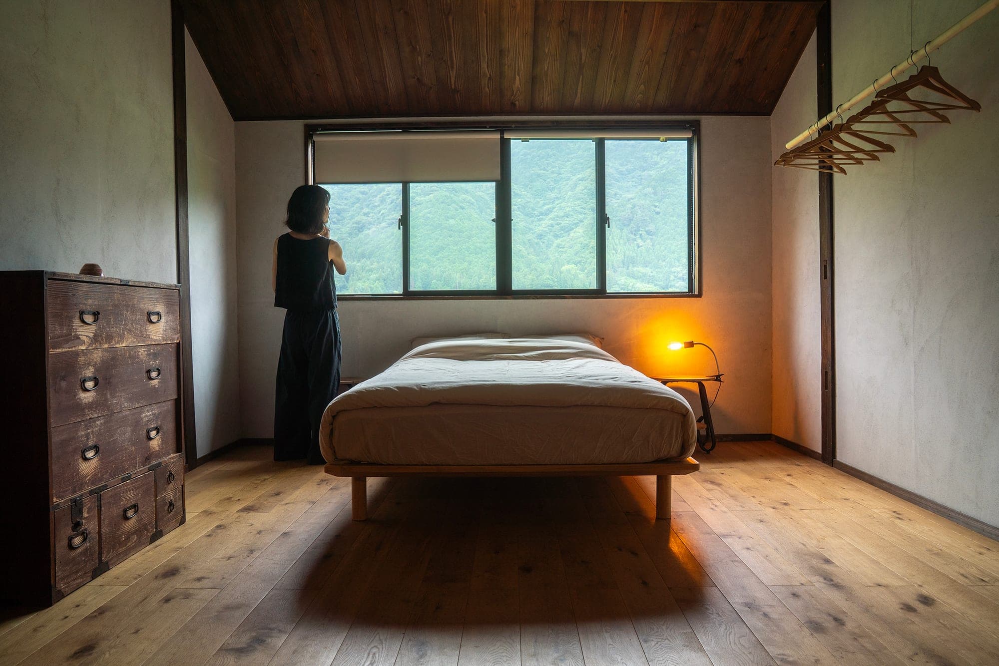 Bedroom with a low wooden bed, antique tansu chest, and a window framing the mountains