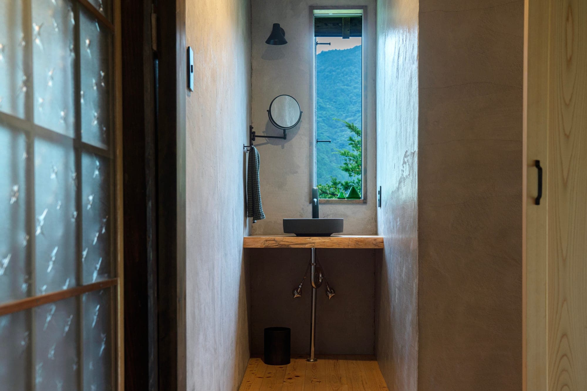 Narrow washroom with a black basin on a wood counter and a window opening to the mountains