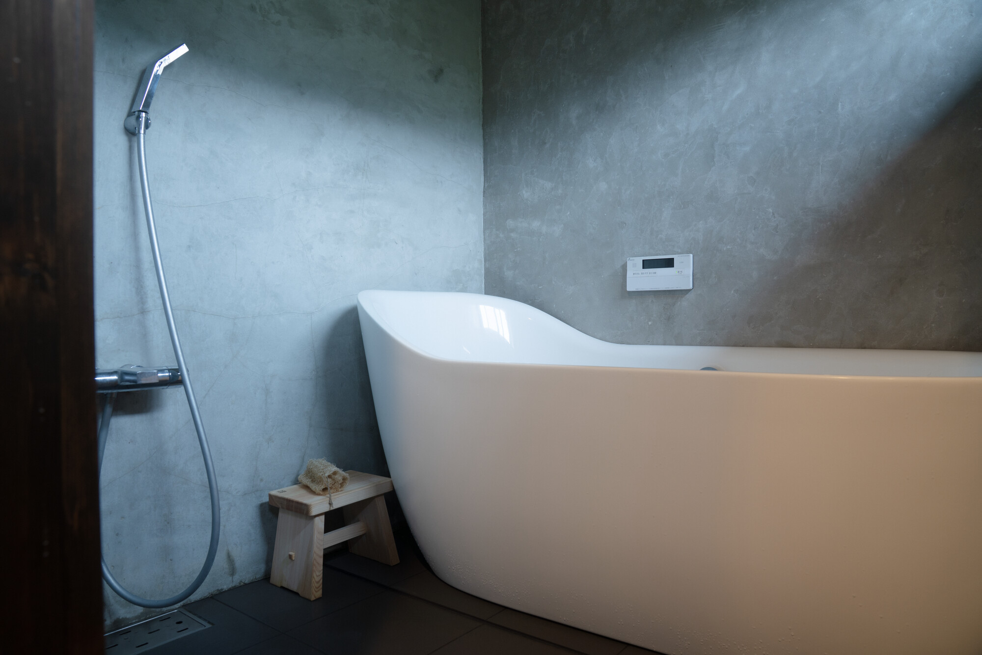 Concrete bathroom with a white freestanding tub and a small wooden stool