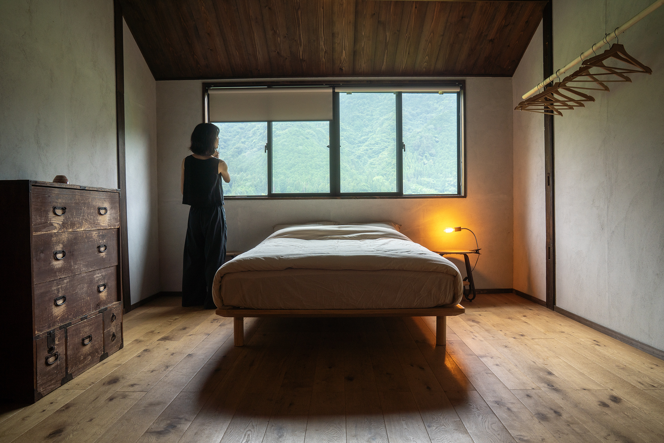 Bedroom with a low wooden bed, antique tansu chest, and a window framing the mountains