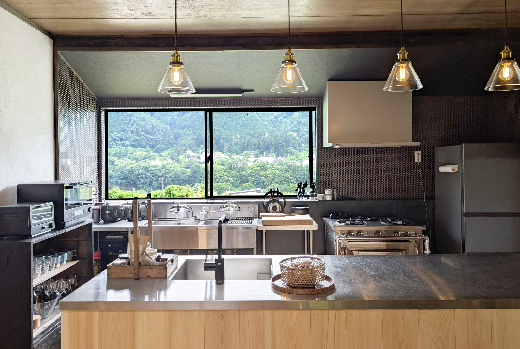 Kitchen with stainless steel counters, pendant lights, and large windows overlooking the forest