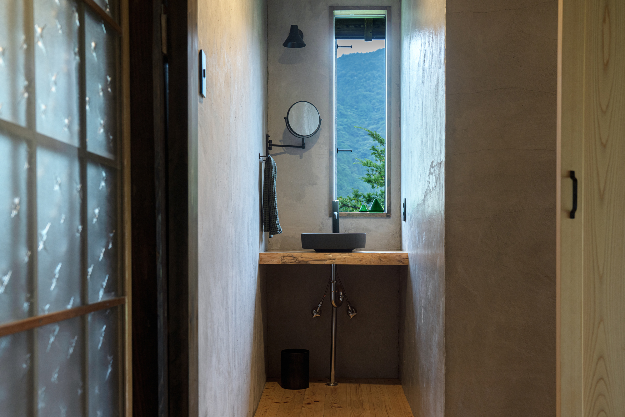 Narrow washroom with a black basin on a wood counter and a window opening to the mountains